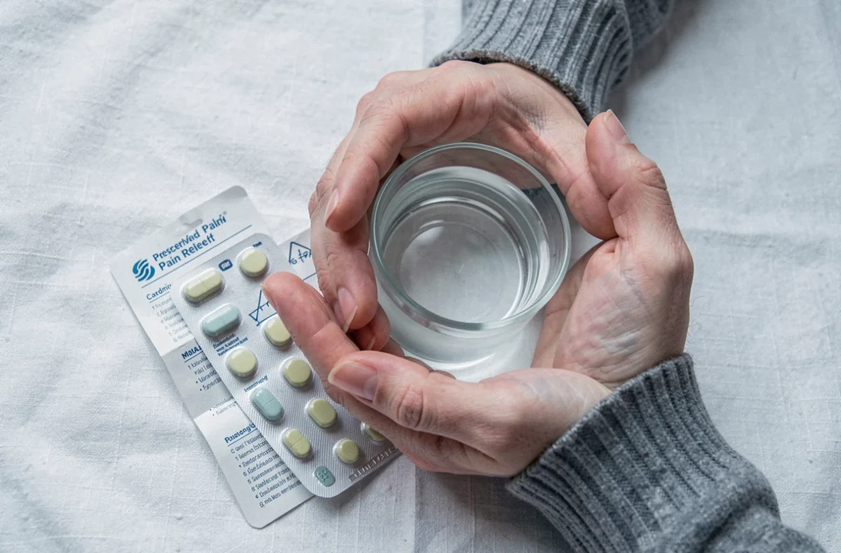 Gros plan sur les soins essentiels après une opération dentaire : médicaments, compresse froide et verre d'eau sur tissu blanc
